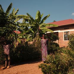 Woman standing in a garden with banana plants and a brick house in the background