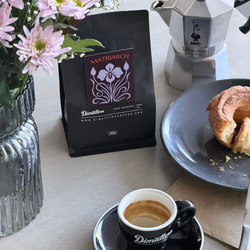 Coffee setup with Matriarch coffee bag, espresso cup, and donut on a table.