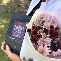 Person holding a bouquet of flowers and a bag of Matriarch coffee