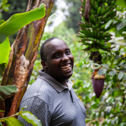 Sam standing amongst banana trees with a smile, surrounded by greenery