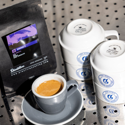 A close up of a shot of espresso with a bag of Ronnie's blend in the background