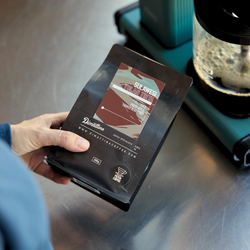 A close up of a bag of Yolan Tirta coffee with a Moccamaster in the background